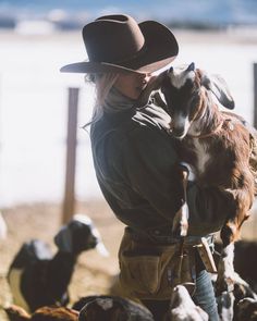 a woman wearing a cowboy hat and holding a dog in her arms while standing next to other dogs