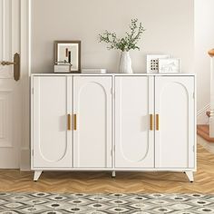 a white cabinet with gold handles in a living room next to a stair case and potted plant