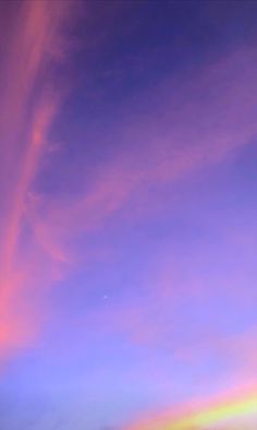 an airplane flying in the air with a rainbow colored sky behind it and some clouds