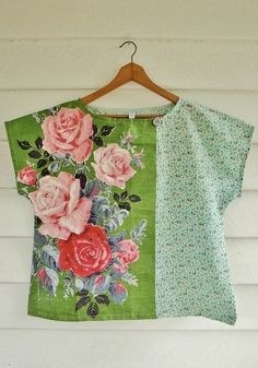 a green top with pink roses on it hanging from a wooden hanger next to a white wall