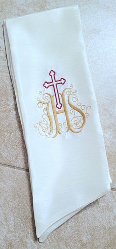 a white towel with a cross on it and the letter j is spelled in gold