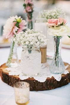 three vases with flowers are sitting on a wood slice at a wedding reception table