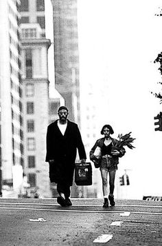 a man and woman walking down the street with suitcases in their hands, carrying flowers