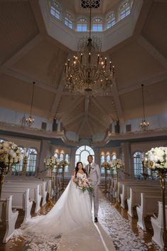 a bride and groom standing in the aisle of a church with chandeliers hanging from the ceiling