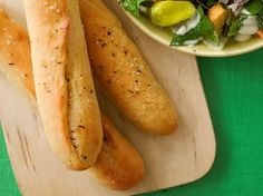 breadsticks and a bowl of salad on a cutting board next to a green tablecloth