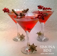 two glasses filled with red liquid and garnished with berries, cinnamon and mist