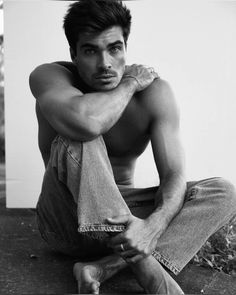 a shirtless man sitting on the ground with his arms crossed and looking at the camera