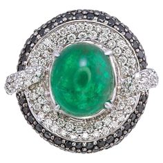 This striking ring features a 9.34-carat cabochon-cut emerald from Zambia, certified by AIG (American International GemLab). With minor treatment, the emerald showcases an appealing green color, making it a captivating centerpiece in this luxurious design. Set in 18K white gold, the emerald is enhanced by 3.62 carats of diamonds. The combination of black diamonds and round white diamonds creates a bold contrast, adding depth and brilliance to the design. The diamonds are artfully arranged to complement the smooth cabochon shape of the emerald, providing a modern yet timeless look. Complimentary resizing and custom engraving services are available, allowing for a personalized touch that ensures the perfect fit and a unique piece. This ring exemplifies fine craftsmanship and distinctive desi Fancy Diamond Ring, Emerald Diamond Ring, Zambian Emerald, Black Diamond Ring, Diamond Cocktail Rings, Cabochon Ring, Fancy Diamonds, 18k Gold Ring, Modern Ring