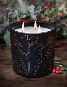 a lit candle sitting on top of a wooden table next to holly and red berries