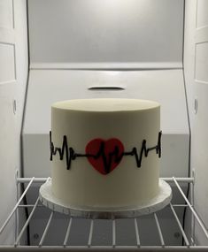 a white cake with a red heart and heartbeat on it in an open oven area