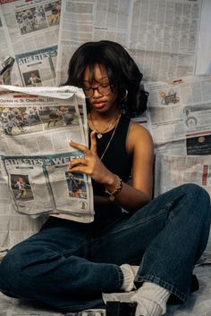 a woman sitting on the floor reading a newspaper while holding her hand up to her face