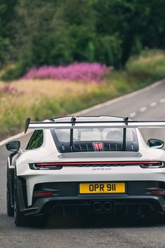 the rear end of a white sports car driving down a road with trees in the background