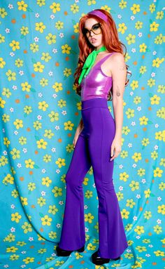 a woman with red hair wearing purple pants and a green top is posing for the camera