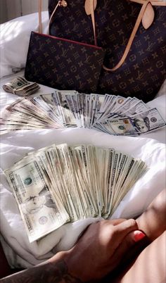 a woman's hand with money and a purse on top of the bed in front of her