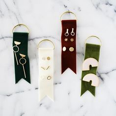 three different colored ribbons with earrings hanging from them on a marble countertop in front of a white marble background