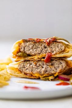 two hamburgers with cheese and ketchup on a white plate next to chips