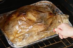 a person is holding a roasting pan with chicken in it and wrapped in plastic