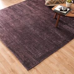 a living room area with hardwood floors and a purple rug on the floor next to a coffee table