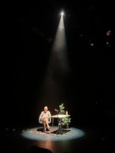 a man sitting at a table in the middle of a stage with a spotlight on him