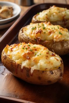 baked potatoes with cheese and parmesan on a wooden serving tray next to a bowl of bread