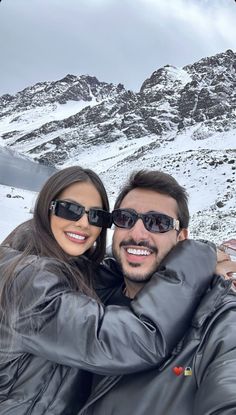 a man and woman taking a selfie in front of snow covered mountains with their arms around each other