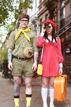 a man and woman dressed in costumes standing next to each other on the sidewalk with luggage