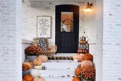 pumpkins and gourds are on the front steps of a house with white brick walls