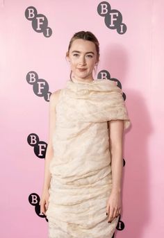 a woman standing in front of a pink wall wearing a dress with ruffles