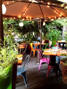 an outdoor dining area with colorful chairs and tables under an umbrella that has lights on it