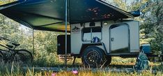 an off - road camper is parked in the woods with its awning open