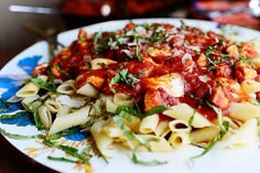 pasta with tomato sauce and herbs on a blue and white plate next to other food