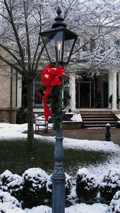 a street light covered in snow with a red bow on it's post and trees