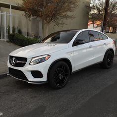 a white mercedes gle is parked on the side of the road in front of a building