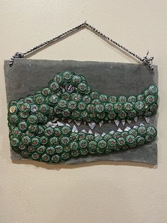 a green and white alligator head made out of soda cans on a gray sign hanging from a wall