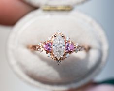 a close up of a person holding an engagement ring in a box with pink and white stones