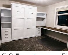 an empty room with white cupboards and drawers next to a large window in the corner