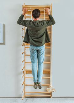 a man standing on top of a wooden ladder in front of a wall mounted clock