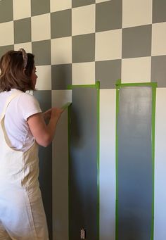 a woman in white overalls painting a checkerboard wall with green tape on it