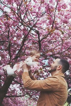 a man holding a baby in front of a tree with pink flowers