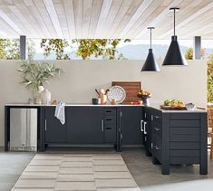 an outdoor kitchen with black cabinets and stainless steel appliances on the countertop, along with potted plants