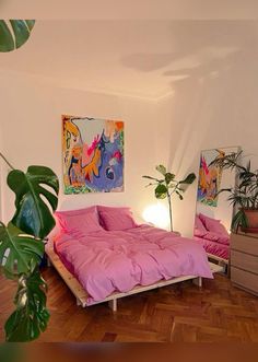 a bedroom with pink bedding and paintings on the wall, wooden flooring and potted plants