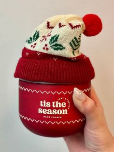 someone is holding up a cup with a knitted hat on top and it says tis the season