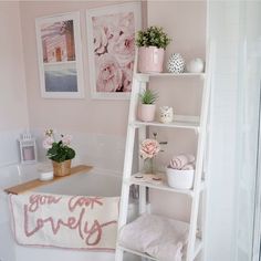 a bathroom with pink walls and white shelving unit holding towels, potted plants and flowers