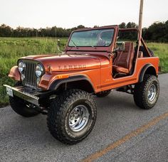 an orange jeep is parked on the side of the road in front of some grass