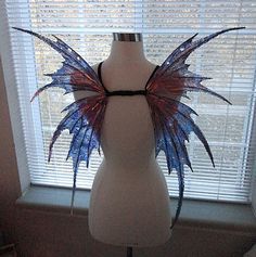 a white mannequin with blue and red wings on it's head stands in front of a window