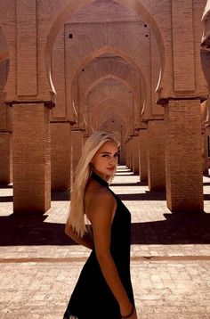 a woman in a black dress is posing for a photo with arches and columns behind her