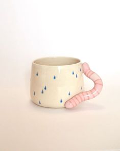 a coffee cup with pink handles and rain drops on it's side, sitting on a white surface