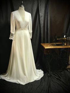 a white dress on display in front of a black backdrop with a sewing machine behind it