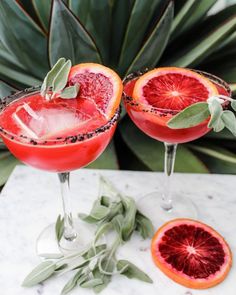 two glasses filled with blood orange margaritas and garnished with sage leaves on a marble table