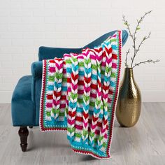 a crocheted blanket sitting on top of a blue chair next to a vase